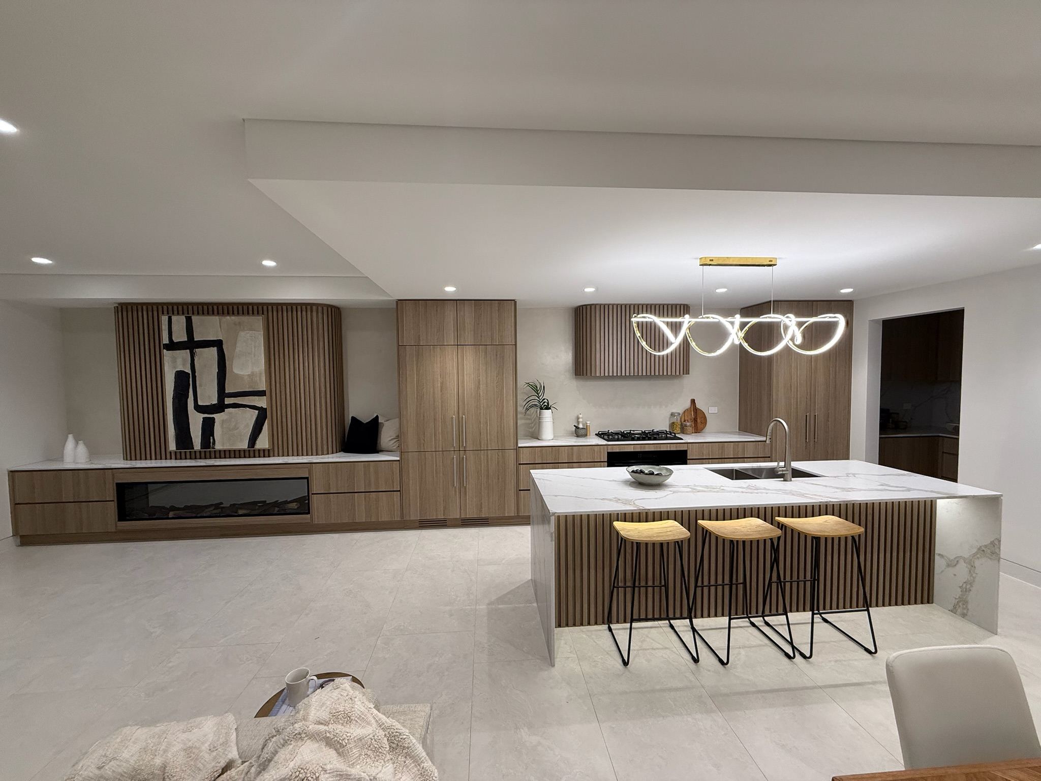 Open-plan kitchen with fluted timber joinery, stone waterfall island and built-in fireplace at Wattle St, Punchbowl
